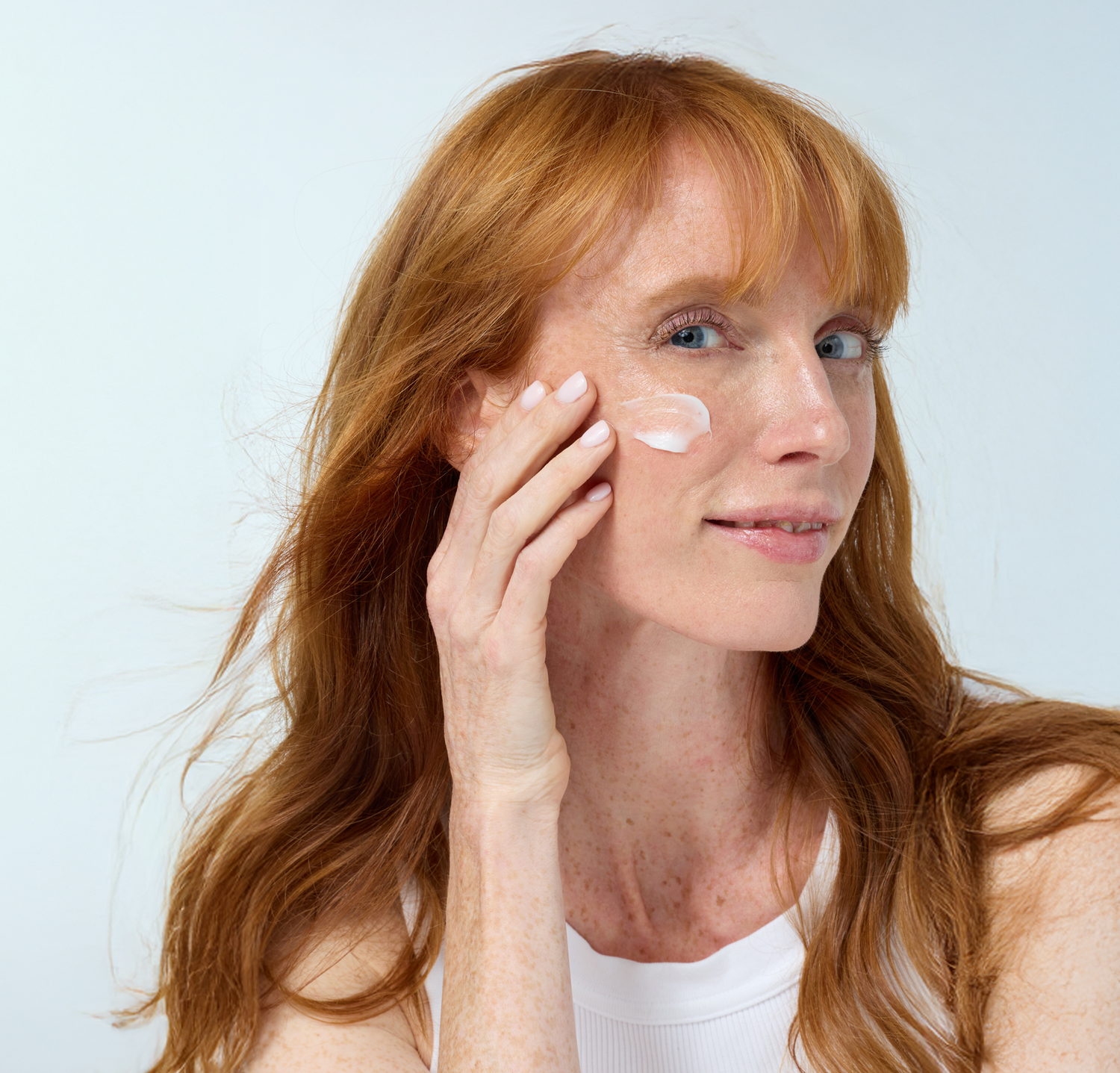Woman applying cream to her face with a blue background